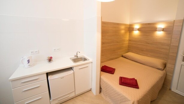 A compact hotel room with a kitchenette, a bed with red towels, and a wooden accent wall. - Smart Apartment Teodora 5a (Lviv)