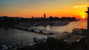 Una vista al atardecer de un río con un puente, barcos y un edificio con una torre.