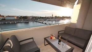 Un balcón con vistas al puerto, un sofá, una mesa con una botella y vasos, y un plato de comida.