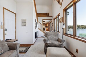 Un salon confortable avec un canapé, un fauteuil et un téléviseur. Un escalier mène à une mezzanine.