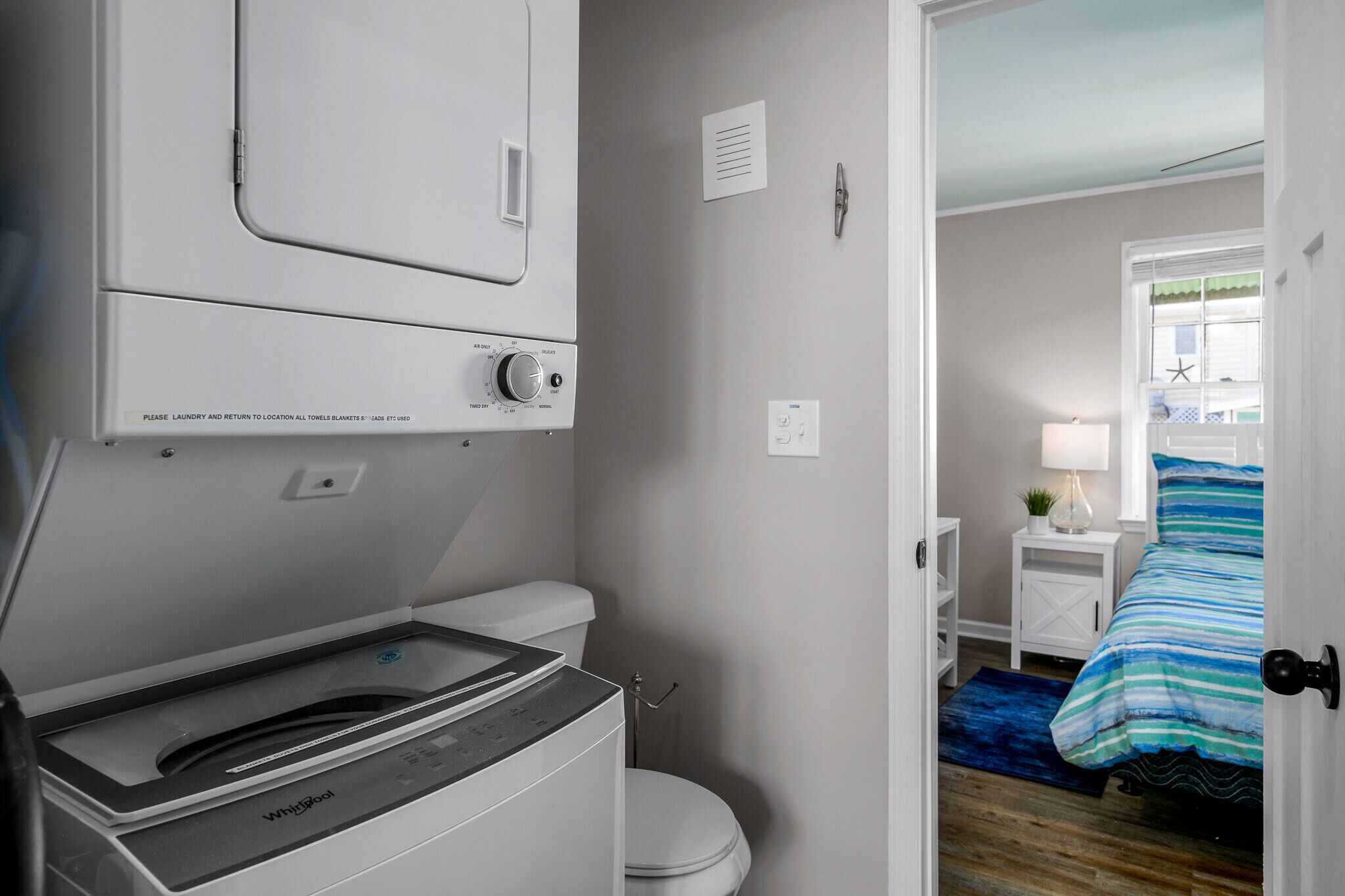 A compact bathroom with a Whirlpool washer and dryer, a white toilet, and a small bedside table with a lamp.