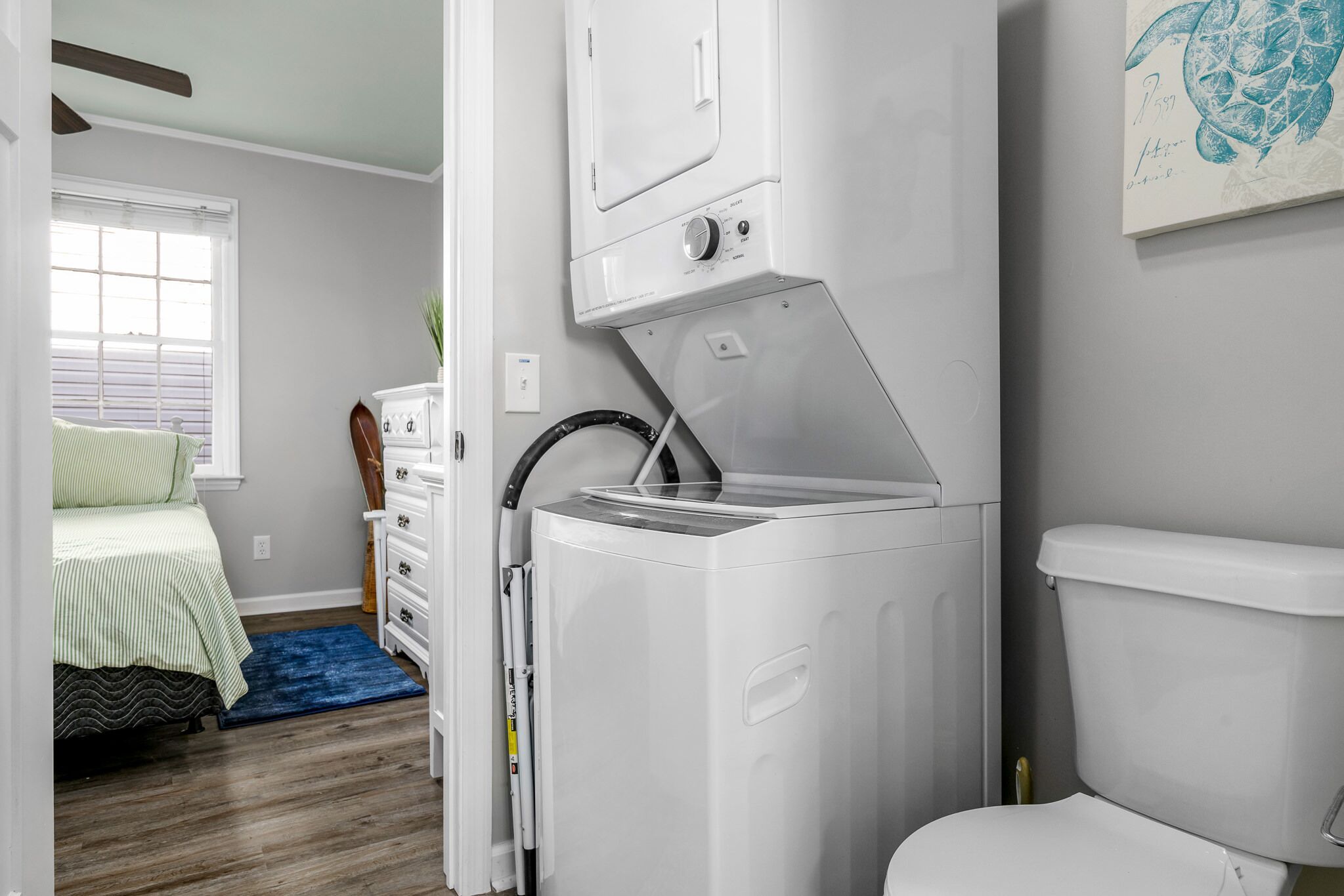 Une buanderie équipée d’un lave-linge et d’un sèche-linge à chargement frontal, un lit avec une literie verte, un tapis bleu et des toilettes blanches.