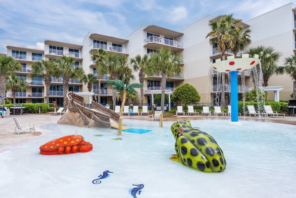 Une piscine d’hôtel avec des toboggans, une fontaine en forme de grenouille et des chaises longues.