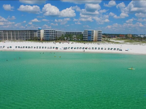 Un hotel frente a la playa con varias edificaciones, una playa de arena y aguas turquesas cristalinas.