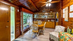 A wooden cabin interior with a dining area, a sofa, and a kitchen with shelves.