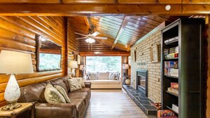 A cozy cabin interior with a leather sofa, a fireplace, and a bookshelf.