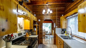 A wooden cabin kitchen with a stove, sink, and dining area.