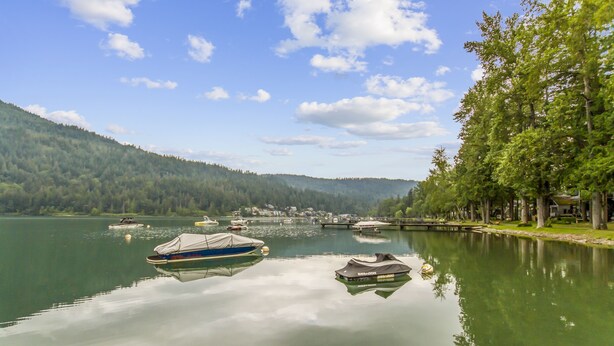 A calm lake with boats, a dock, and a forested hillside.