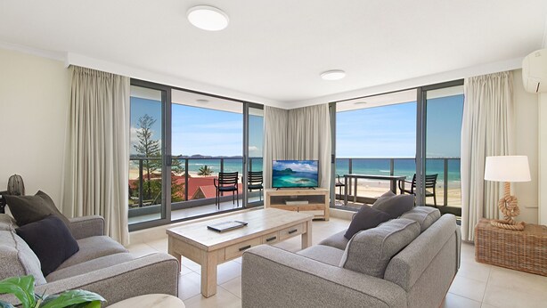 A modern hotel room with a large balcony, a flat-screen TV, and a comfortable seating area with a view of the beach. - Kirra Gardens 17 - Kirra Point Beachfront (Coolangatta)