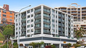 A multi-story hotel with balconies, named 'Kirra Gardens,' featuring a modern architectural design with a prominent central column. - Kirra Gardens 17 - Kirra Point Beachfront (Coolangatta)