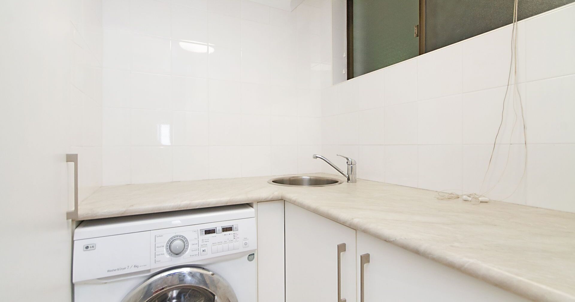 A compact kitchen with a washing machine, a sink, and a window above the sink.