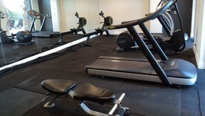 Een fitnessruimte met trainingsapparatuur, waaronder loopbanden en krachtapparaten, en een grote spiegel die de ruimte weerspiegelt.