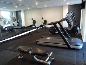 Un gimnasio con equipo de ejercicio, incluyendo cintas de correr y máquinas de pesas, y un espejo grande que refleja el espacio.