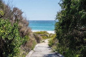 A wooden pathway leading to a beach with clear skies and ocean views.