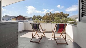 Een balkon met twee gestreepte stoelen en uitzicht op huizen en bomen.