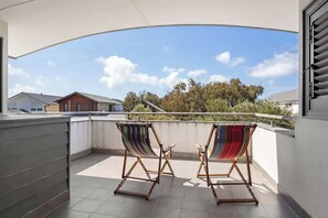 Un balcón con dos sillas a rayas y vista a casas y árboles.