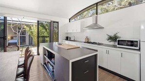 Een moderne keuken met een groot eiland, witte kasten en uitzicht door grote ramen.