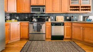 A kitchen with wooden cabinets, a microwave, stove, oven, dishwasher, and a patterned rug. - Loft Over Broadway Strip (Nashville)