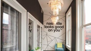 A modern hallway with a green sofa, a blue armchair, and a chandelier. - Loft Over Broadway Strip (Nashville)