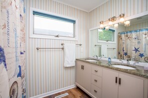 A bathroom with striped wallpaper, a window, a towel rack, a sink, and a vanity with drawers.