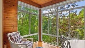 A room with large windows, a wooden ceiling, and a white chair with a patterned cushion. - Midtown Riverfront Condo Extended Stays (Traverse City)