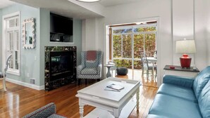 A living room with a fireplace, a blue sofa, a white coffee table, and a television. - Midtown Riverfront Condo Extended Stays (Traverse City)