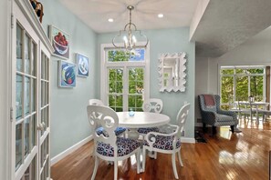 A dining area with a round table and white chairs, a chandelier, and artwork on the walls.