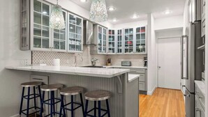 A modern kitchen with a central island, bar stools, stainless steel appliances, and a decorative chandelier. - Midtown Riverfront Condo Extended Stays (Traverse City)