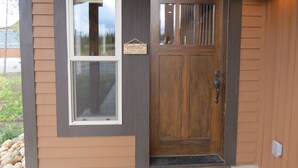 L’entrée d’un chalet en bois, avec une fenêtre et une porte, une pancarte de bienvenue et une lumière sur le porche.