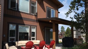 Une maison moderne à deux étages dotée d’un patio couvert, avec des chaises rouges et un canapé beige.
