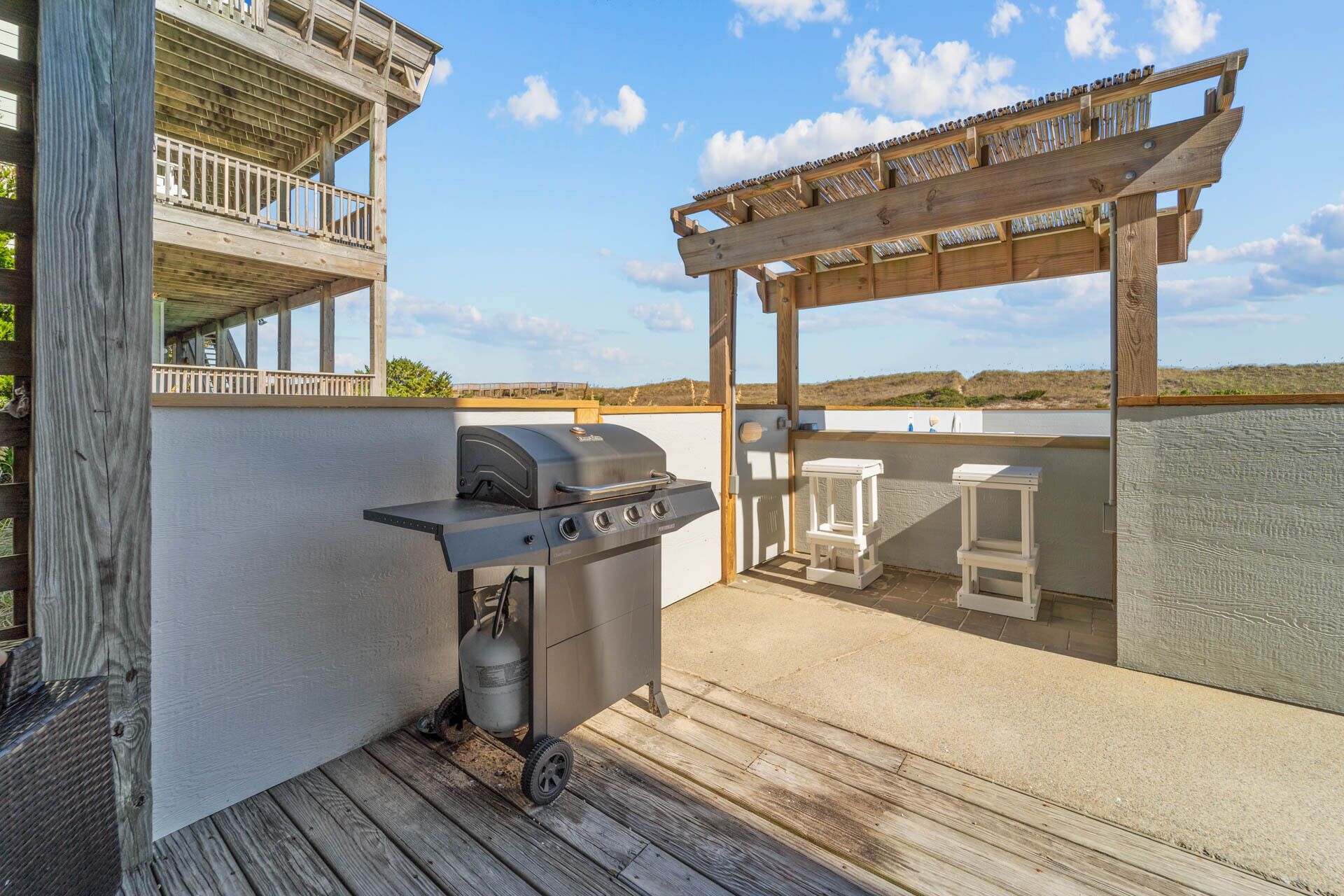 An outdoor patio with a barbecue grill, a gas tank, and a pergola with seating.