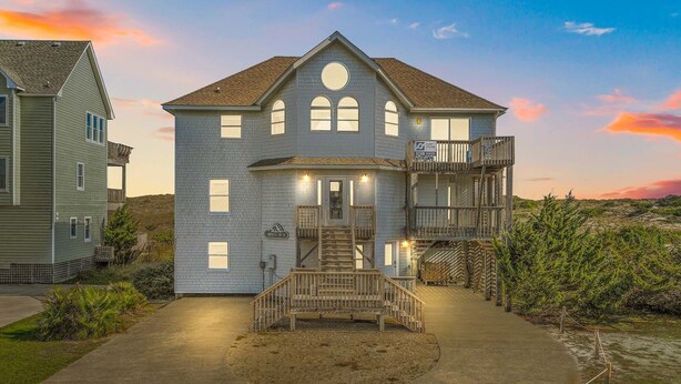 A two-story house with a balcony, a front porch, and a driveway. - Oceanfront Home w/ Pool, Hot Tub, Game Room, Tiki Bar, Community Pool and Tennis (Waves)