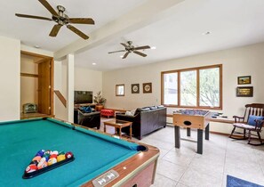 A pool table, two ceiling fans, a foosball table, a sofa, and a window with a view.