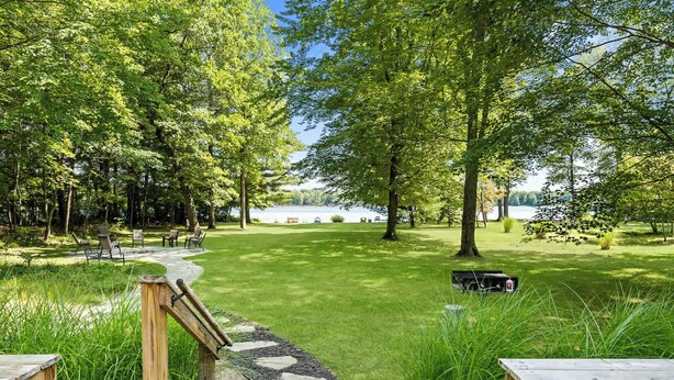 A serene outdoor area with a stone pathway leading to a grassy lawn, surrounded by trees and a body of water in the background. - Peaceful Lakefront Home with Amazing Outdoor Space (Pullman)