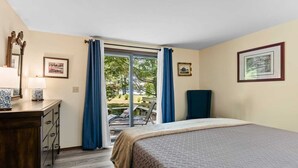 A bedroom with a bed, a dresser, a chair, and a view of the outdoors through a glass door. - Peaceful Lakefront Home with Amazing Outdoor Space (Pullman)