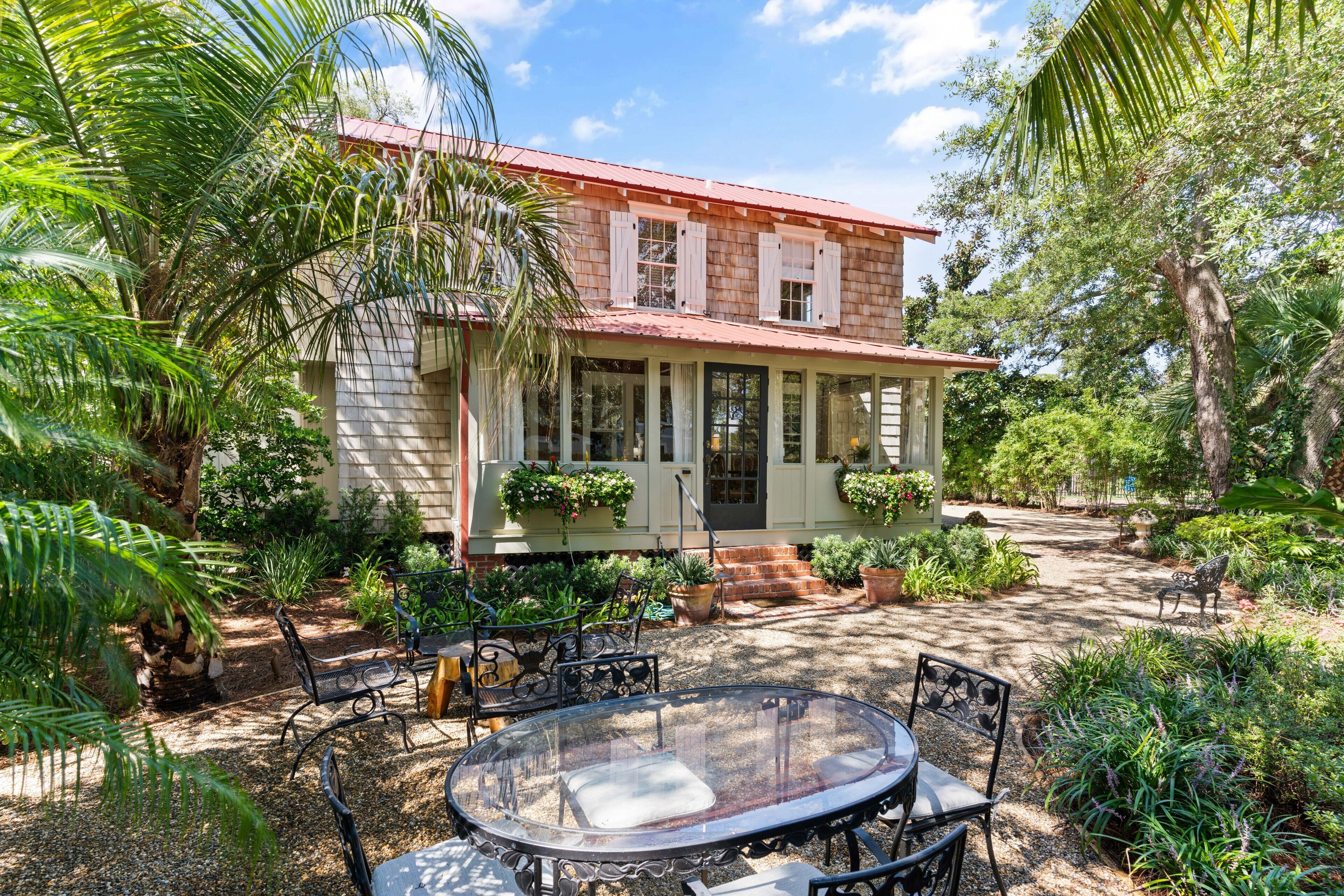 A house with a porch, surrounded by lush greenery and a patio with outdoor furniture.