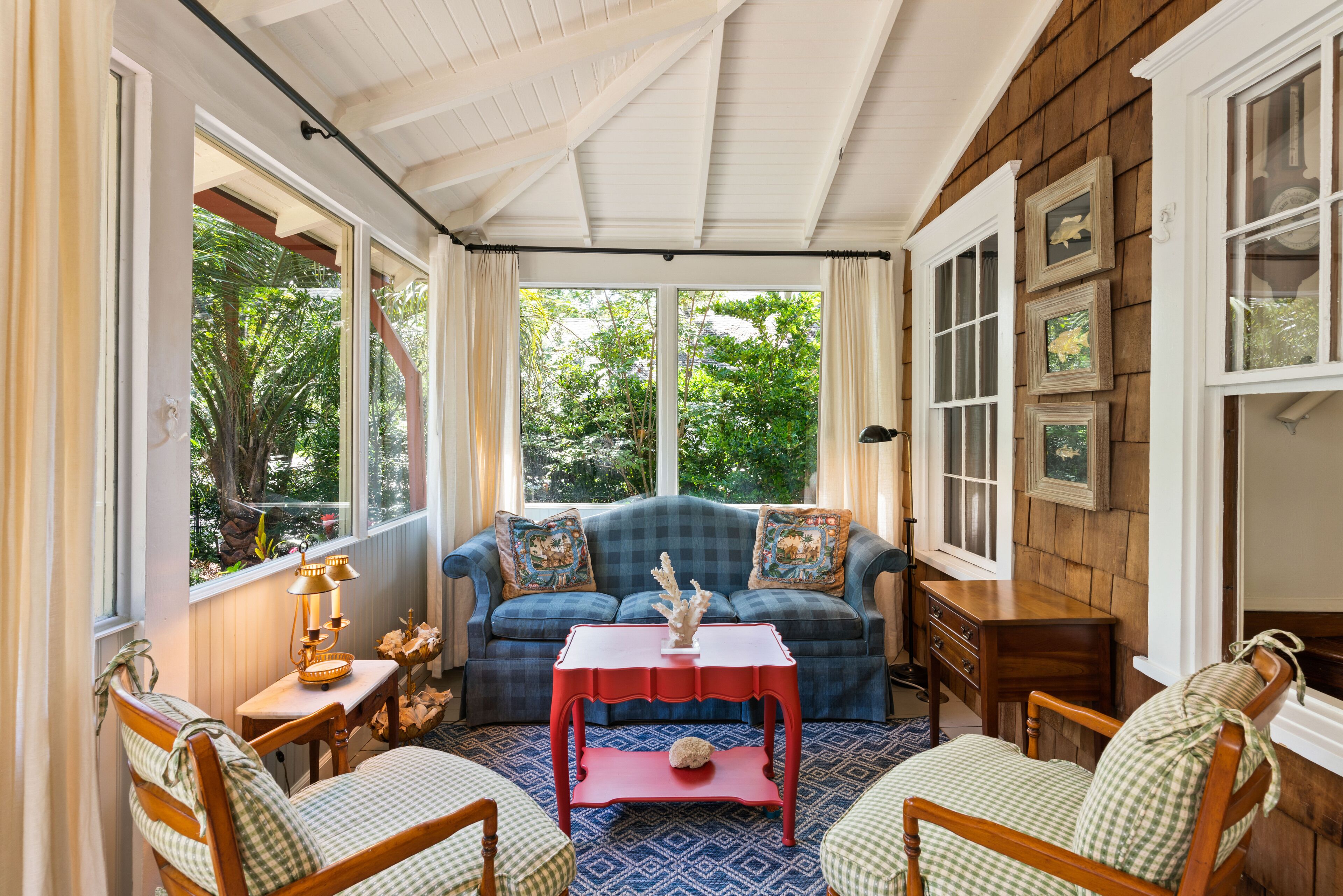 A cozy room with a blue sofa, two wooden chairs, a red table, and a window with curtains.