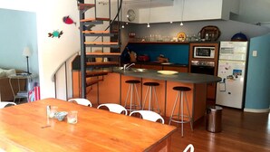 Een compacte keuken met een centraal eiland, barkrukken, een eettafel en een trap.
