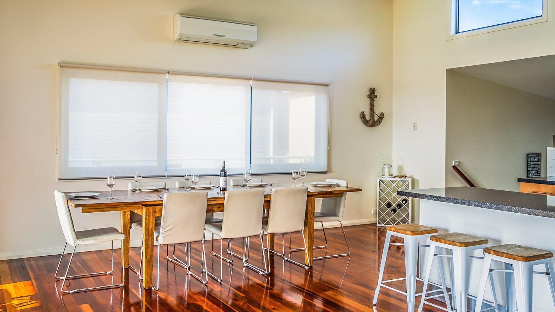 Una cucina moderna con zona pranzo, pavimento in legno e un'ampia finestra con tende.