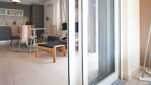 A modern living room with a dining area, a sofa, and a large sliding glass door leading to a balcony. - Olive Village (Sithonia)