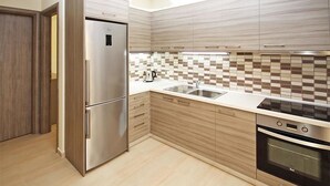 A modern kitchen with a stainless steel refrigerator, a built-in oven, and a tiled backsplash. - Olive Village (Sithonia)