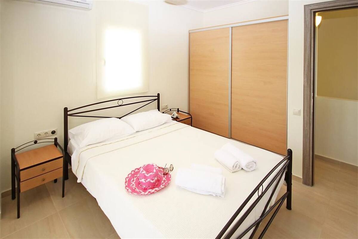 Una cama individual con cabecera de madera, una mesita de noche, un armario y la puerta del baño.