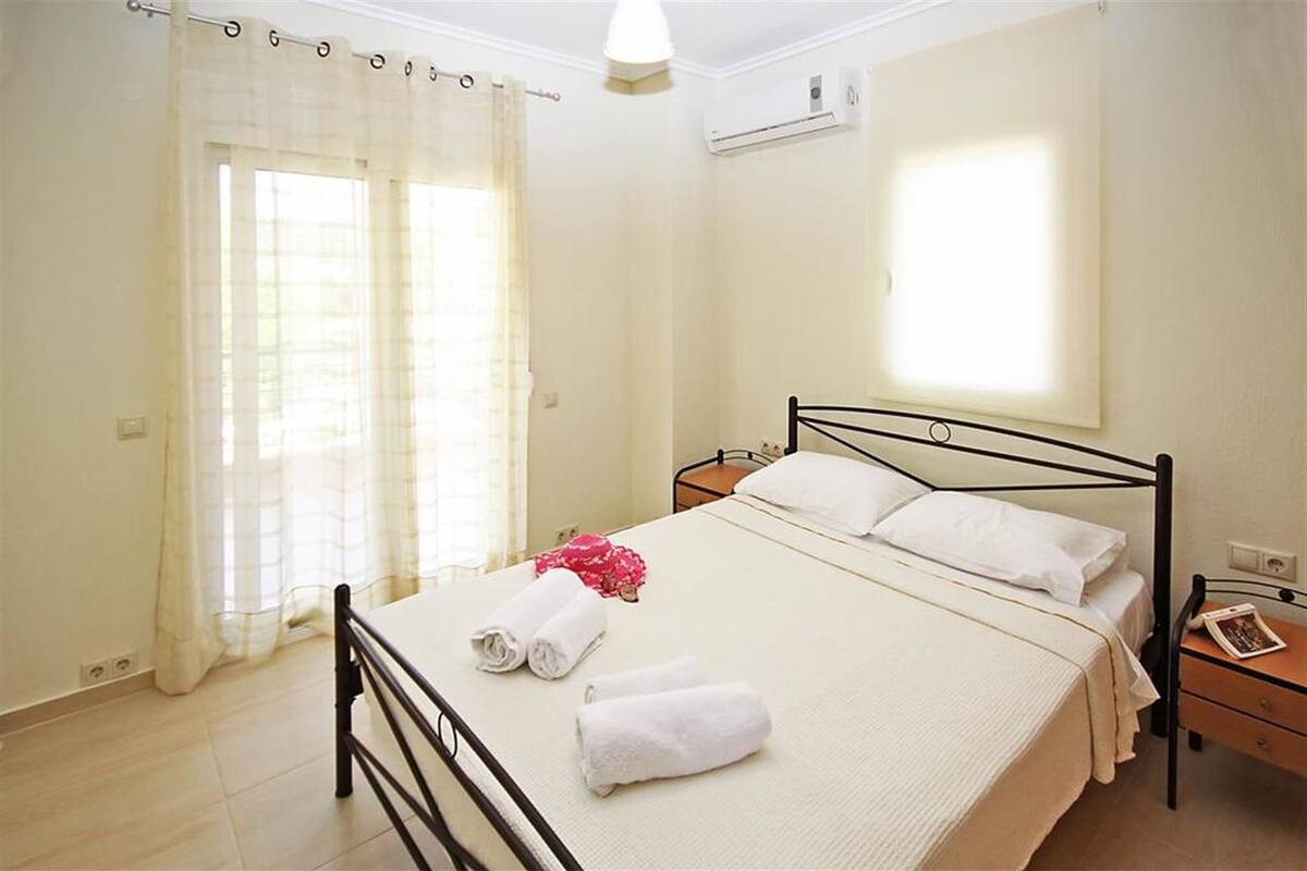Un dormitorio con cama, mesita de noche, ventana con cortinas y equipo de aire acondicionado.
