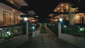 A nighttime view of a hotel corridor with multiple floors, each featuring balconies and illuminated windows. - Olive Village (Sithonia)