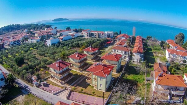 A coastal residential area with houses featuring red-tiled roofs, surrounded by greenery and a clear view of the sea. - Olive Village (Sithonia)