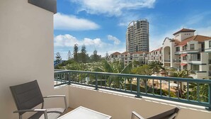 A balcony with a view of a tall building, palm trees, and other residential buildings.