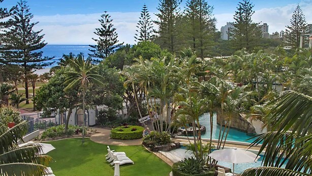 A lush resort with a swimming pool, palm trees, and a view of the ocean.