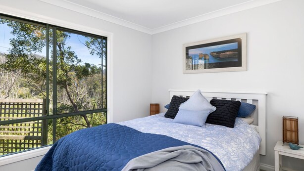 A bedroom with a large window, a bed with a blue quilt, and a framed picture on the wall.