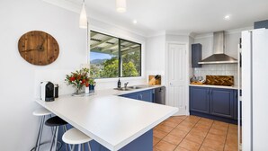 A modern kitchen with a large island, bar stools, a wooden clock, and a view of the outdoors.