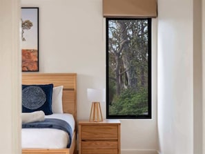 A bedroom with a bed, a nightstand, a lamp, a window with a forest view, and a framed picture on the wall. - Big Rock Dreaming—Bush Retreat w/ Stylish Comforts (Quedjidup)